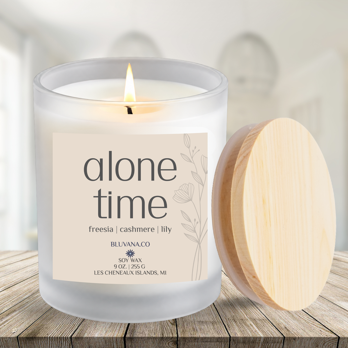 Image of a white frosted glass vessel with flame burning sitting on a wood countertop.  Label is a creamy beige that reads Alone Time with scent notes of freesia, cashmere and ily.