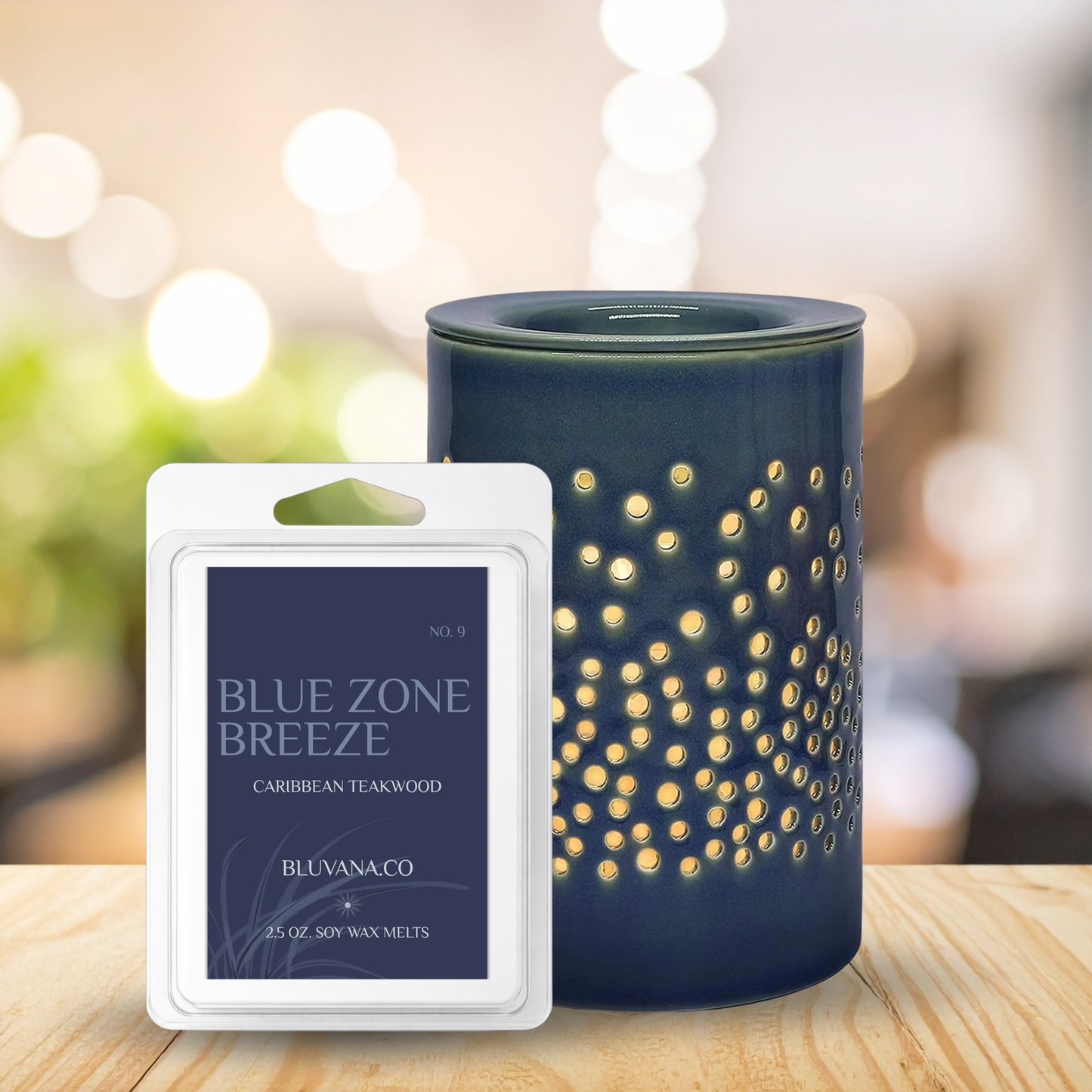 Blue Zone Breeze wax melt packaging and diffuser on a wooden surface with blurred lights in the background