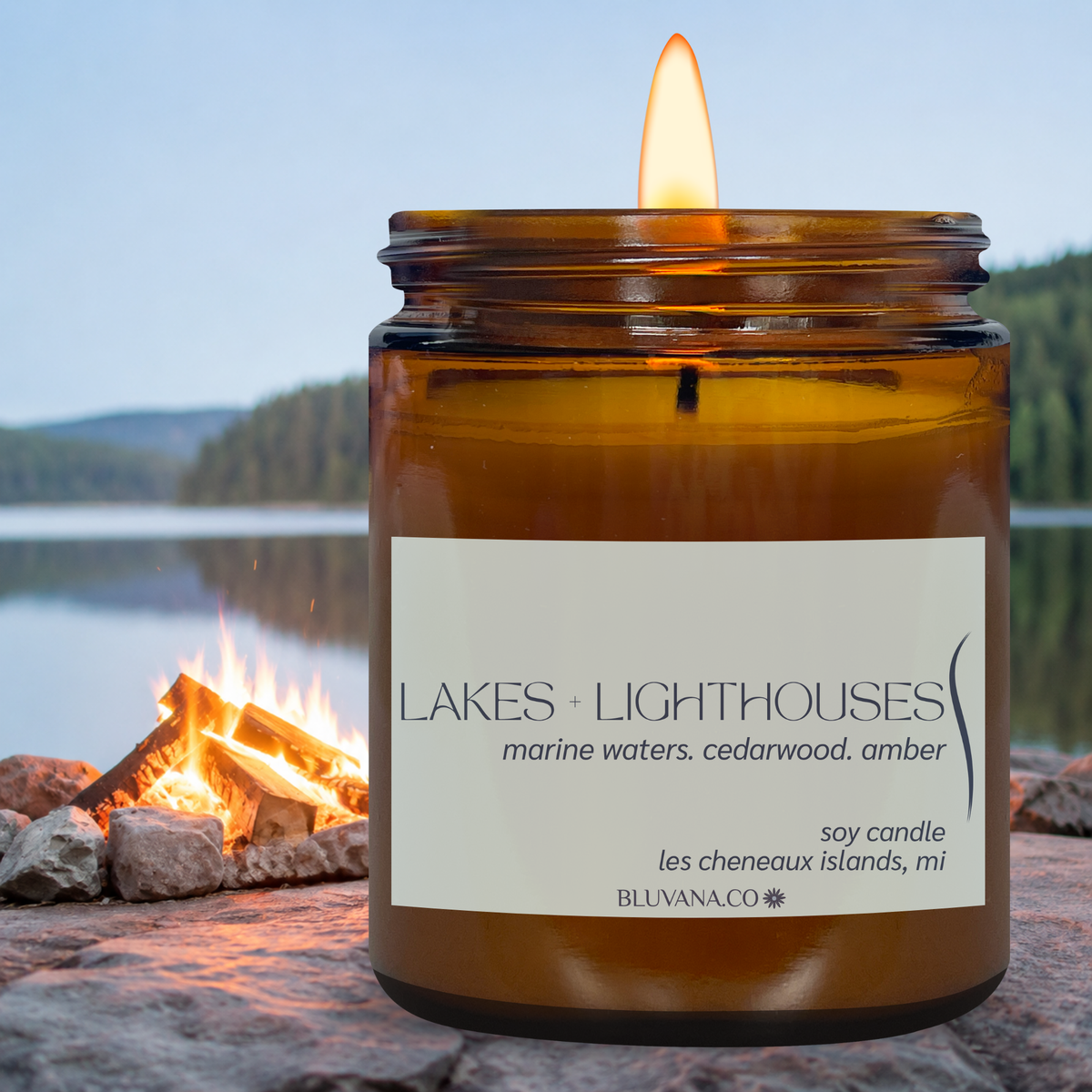 Amber jar candle with a light blue label that says Lakes and Lighthouses featuring an aquatic, cedarwood and amber fragrance. Situated on a rock beach with a lake in the background 