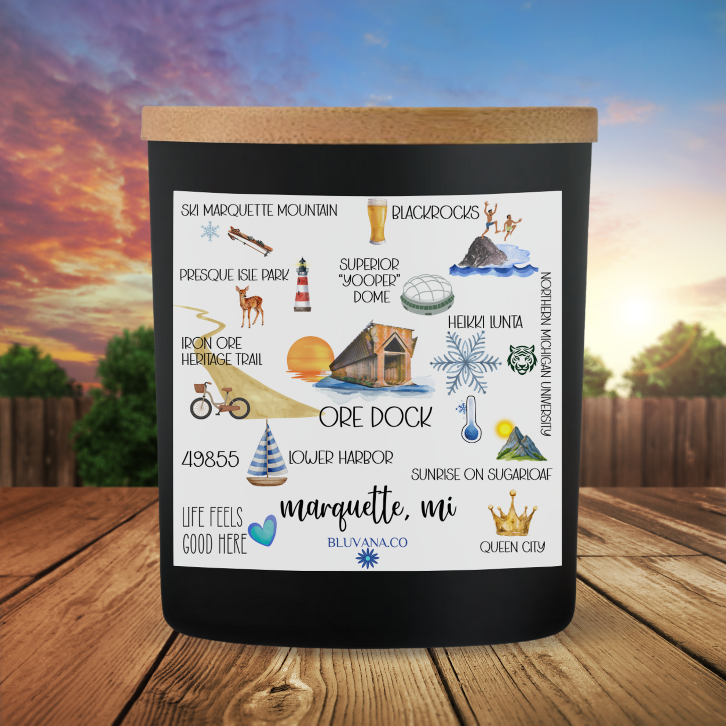 Black candle with illustrations and text on a wooden surface with a scenic background
