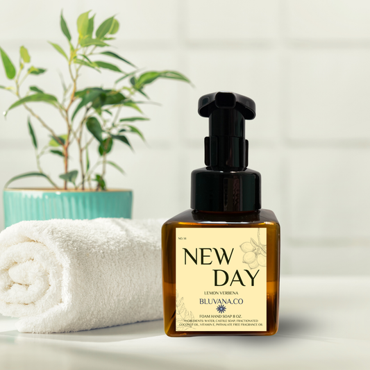 Bottle of 'New Day' soap with a plant and towel in the background