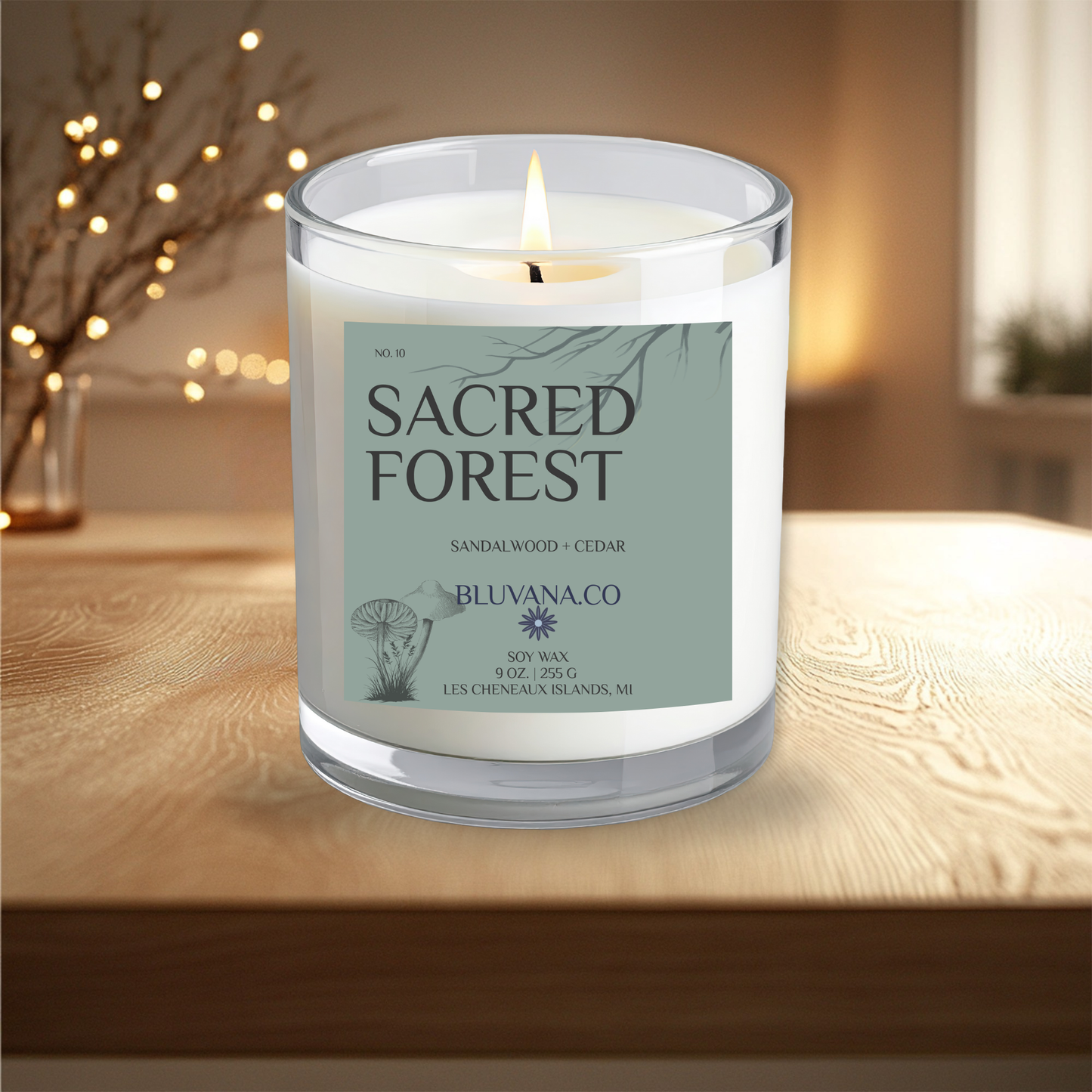 Candle labeled 'Sacred Forest' by Bluvana.co on a wooden surface with blurred lights in the background.