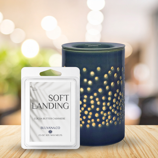 Blue wax melt burner with decorative design next to a 'Soft Landing' wax melt package on a wooden surface.
