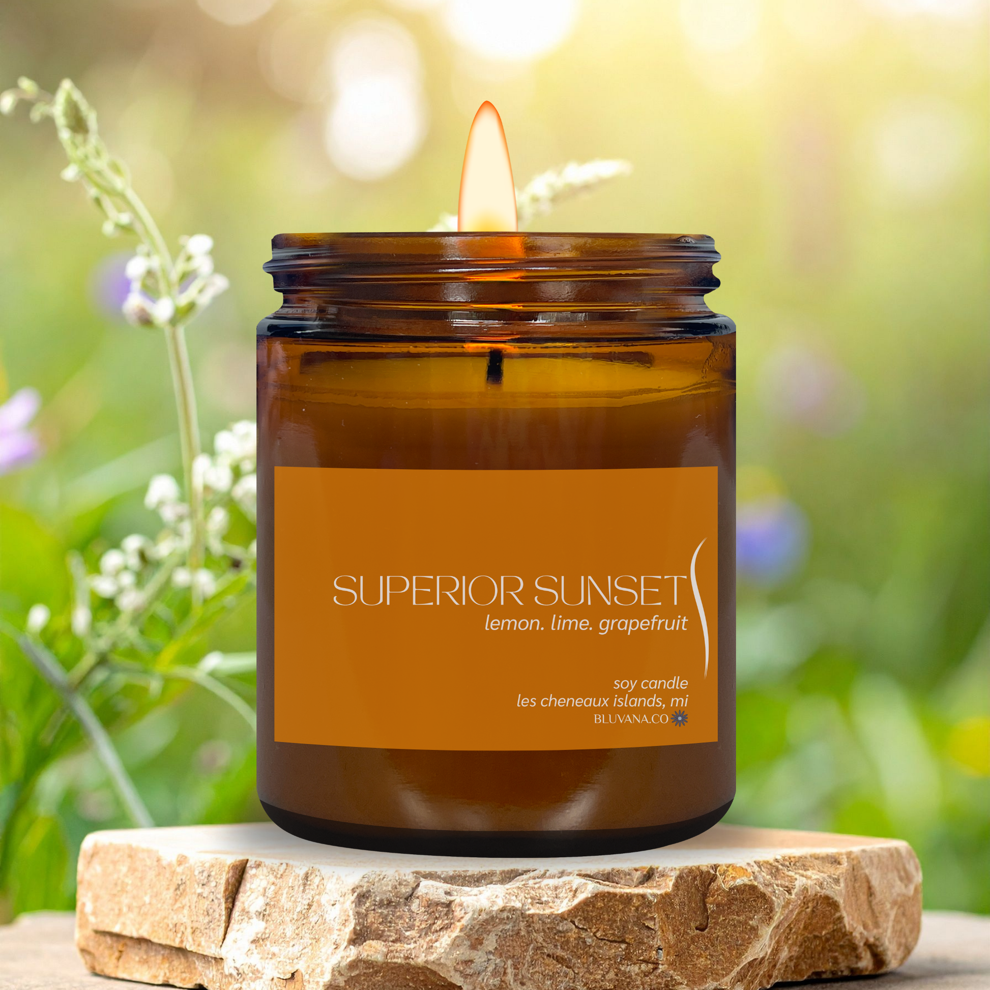 Candle in an amber jar labeled 'Superior Sunset' on a stone surface with a natural background