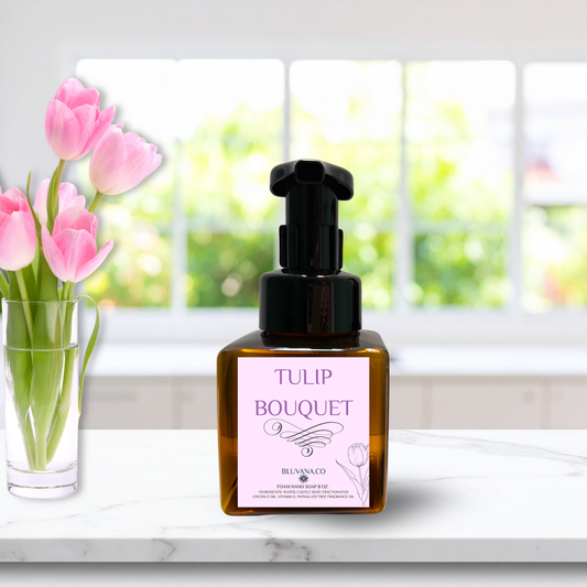 Tulip Bouquet Foam Hand Soap bottle with pink label sitting on a white kitchen counter with a clear vase of pink tulips in the background. 