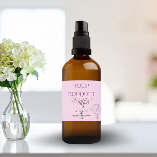 Room Spray in an amber color glass bottle with a pink label that reads Tulip Bouquet with a bouquet of flowers sitting next to it. 