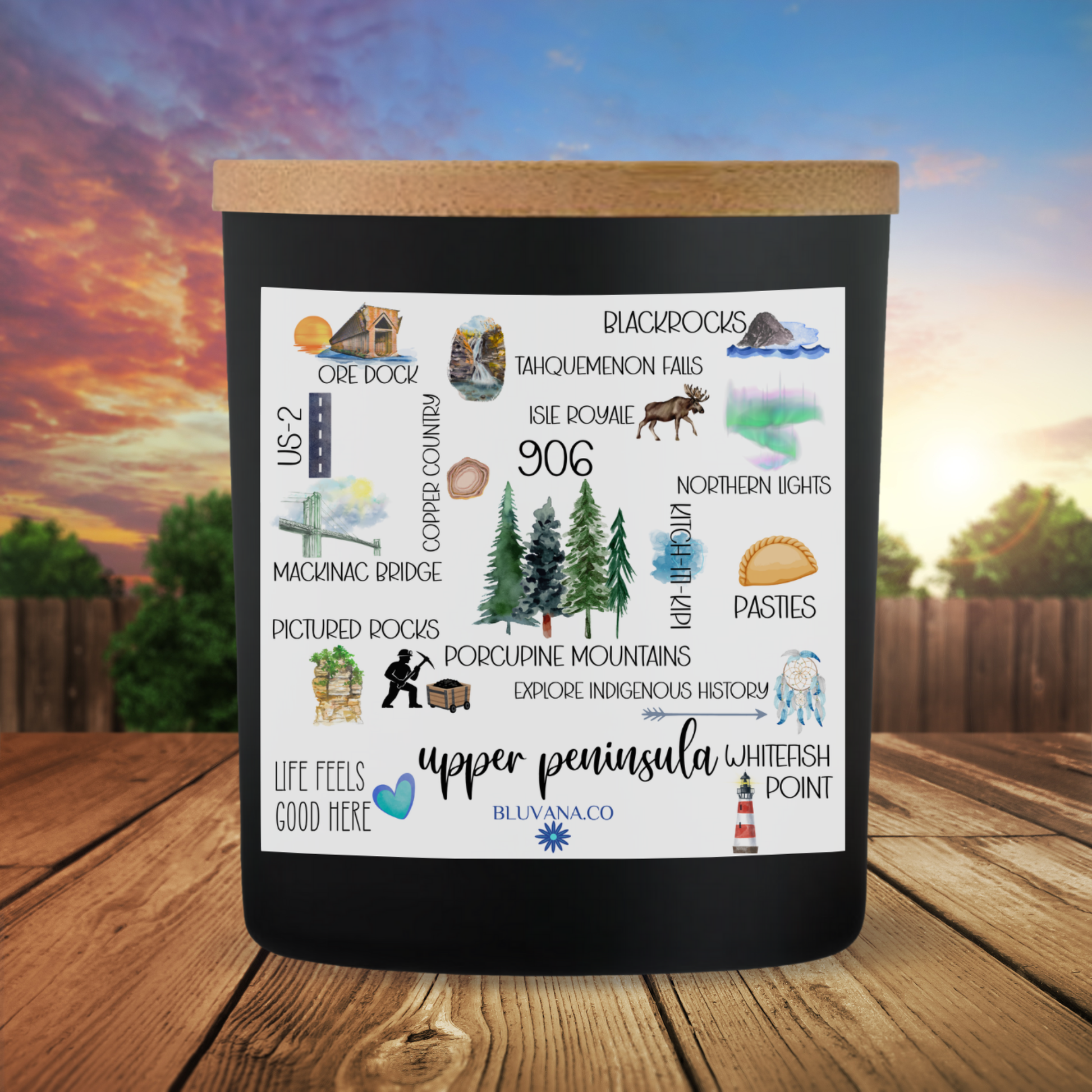 Black candle with illustrations and text on a wooden surface with a scenic background